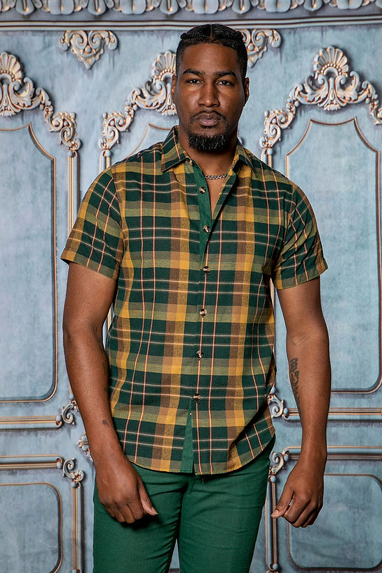 A man showcases the Manzini MANZINI MZL-302 2PC Plaid Linen Shirt Set in Heather Green, featuring a short-sleeve green and yellow shirt with matching pants, making it a stylish addition to any casual wardrobe.