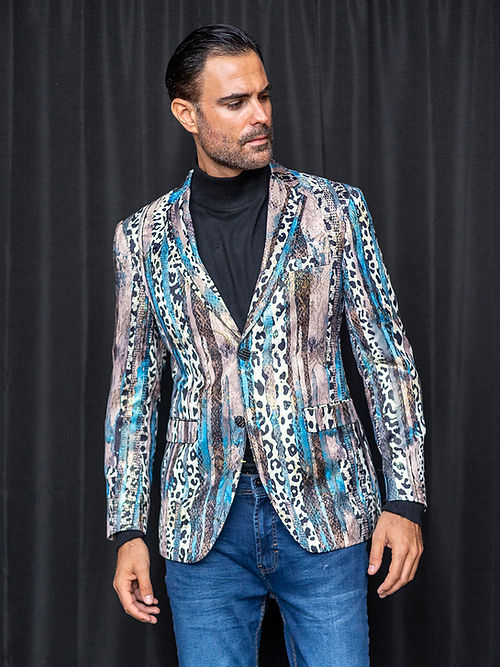 A man wearing a Manzini MANZINI MZS-559 Men's Tailored-Fit Leopard/Reptile Sport Coat Jacket Blazer Blue, a black turtleneck, and blue jeans stands in front of a black curtain.