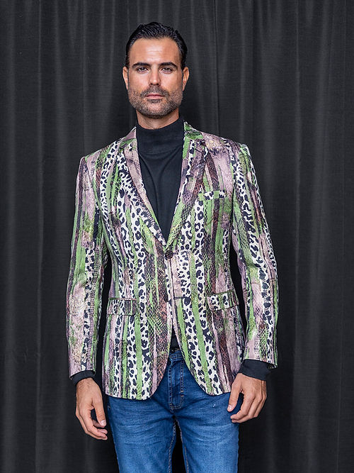 A man stands before a black curtain, wearing the Manzini MZS-559 Men's Tailored-Fit Leopard/Reptile Sport Coat Jacket Blazer Green with a black turtleneck and blue jeans.