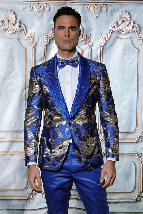 Dressed in the MANZINI MZS-601 Metallic Pattern Rhinestone Tuxedo Suit Royal Jacket, an individual exudes confidence against an ornate backdrop, the suit's shimmering metallic threads beautifully catching the light.