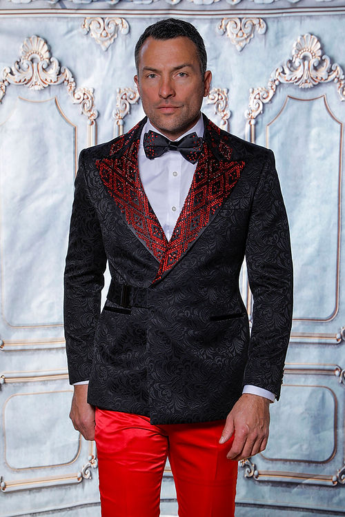 A man in a MANZINI MZS-603 shiny rhinestone floral pattern black/red jacket with red embellishments, paired with red pants, stands before an ornate backdrop.