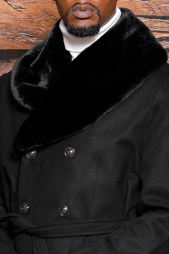 A man stands before a wood-paneled wall wearing the Manzini MZW-322 Black 3/4 Double Breast Winter Coat, featuring a faux fur collar and belted waist.