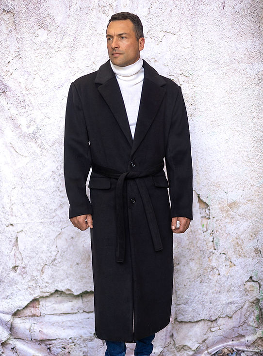A man stands against a textured wall wearing an Insomnia MANZINI MZW-500 black full-length soft fabric trench coat and a white turtleneck.