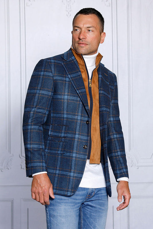 A man in an Insomnia MANZINI MZW-535 indigo plaid blazer coat with a tailored fit, white turtleneck, brown vest, and jeans stands against a light-patterned wall, looking to the side.