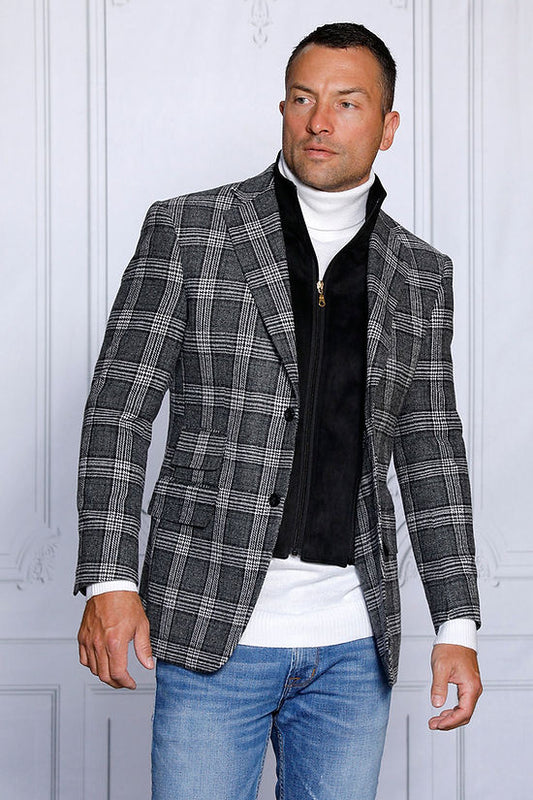 A man stands in front of a gray paneled wall wearing an Insomnia MANZINI MZW-536 black tailored fit faux wool plaid blazer with a zip-out liner over a white turtleneck and zippered vest, paired with blue jeans.