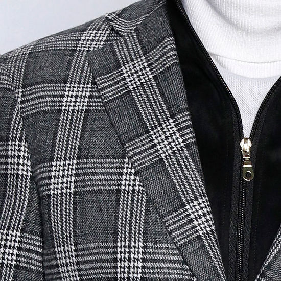 A man stands in front of a gray paneled wall wearing an Insomnia MANZINI MZW-536 black tailored fit faux wool plaid blazer with a zip-out liner over a white turtleneck and zippered vest, paired with blue jeans.