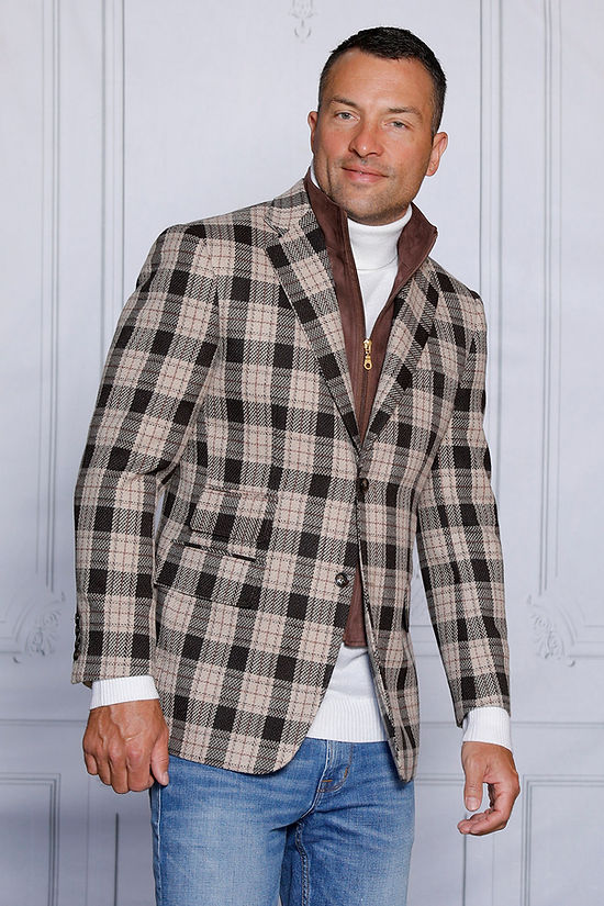 A man wearing the Insomnia MANZINI MZW-536 brown tailored fit faux wool plaid blazer coat with a zip-out liner and a white turtleneck is paired with blue jeans, standing against a light gray, textured backdrop.