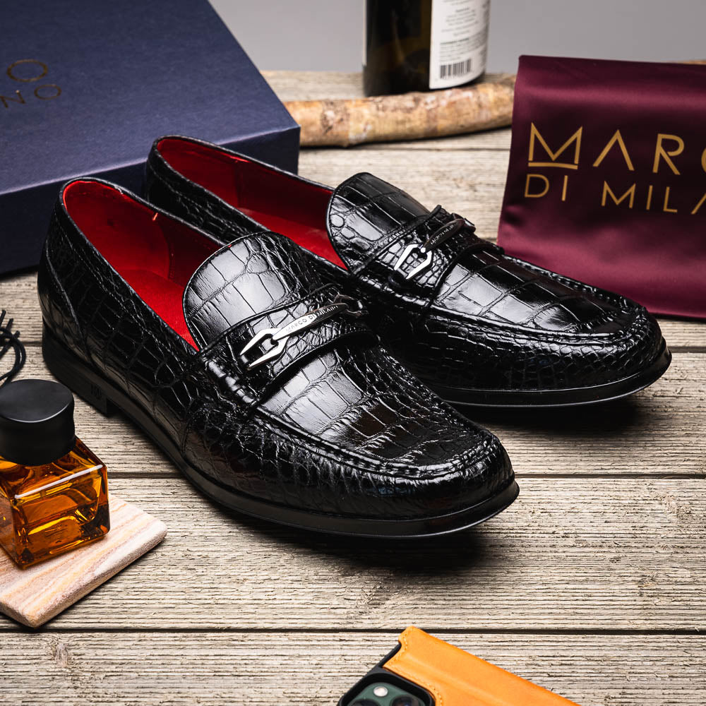 The Milan Black by Marco Di Milano is a black crocodile-pattern leather loafer with a metallic logo detail on the strap and red interior lining, epitomizing luxury men’s footwear.
