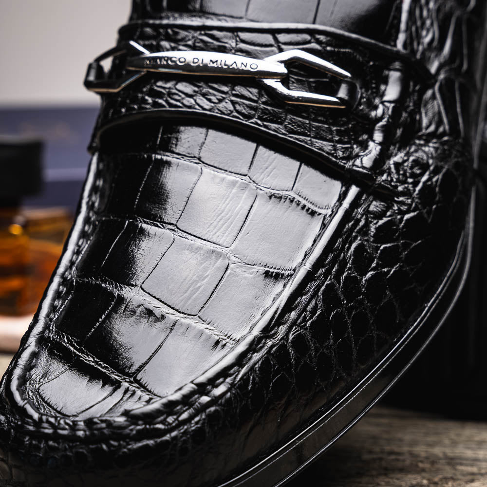 The Milan Black by Marco Di Milano is a black crocodile-pattern leather loafer with a metallic logo detail on the strap and red interior lining, epitomizing luxury men’s footwear.