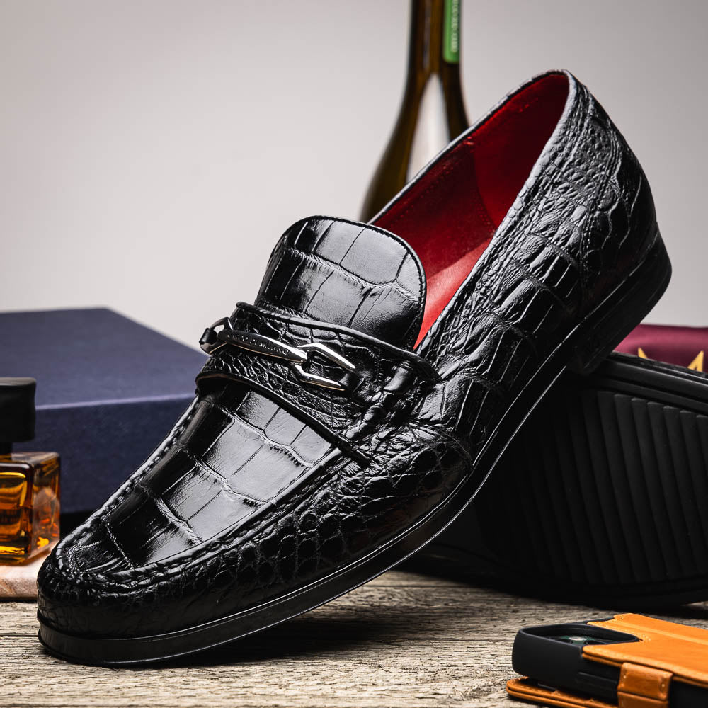 The Milan Black by Marco Di Milano is a black crocodile-pattern leather loafer with a metallic logo detail on the strap and red interior lining, epitomizing luxury men’s footwear.