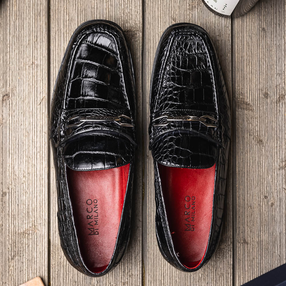 The Milan Black by Marco Di Milano is a black crocodile-pattern leather loafer with a metallic logo detail on the strap and red interior lining, epitomizing luxury men’s footwear.