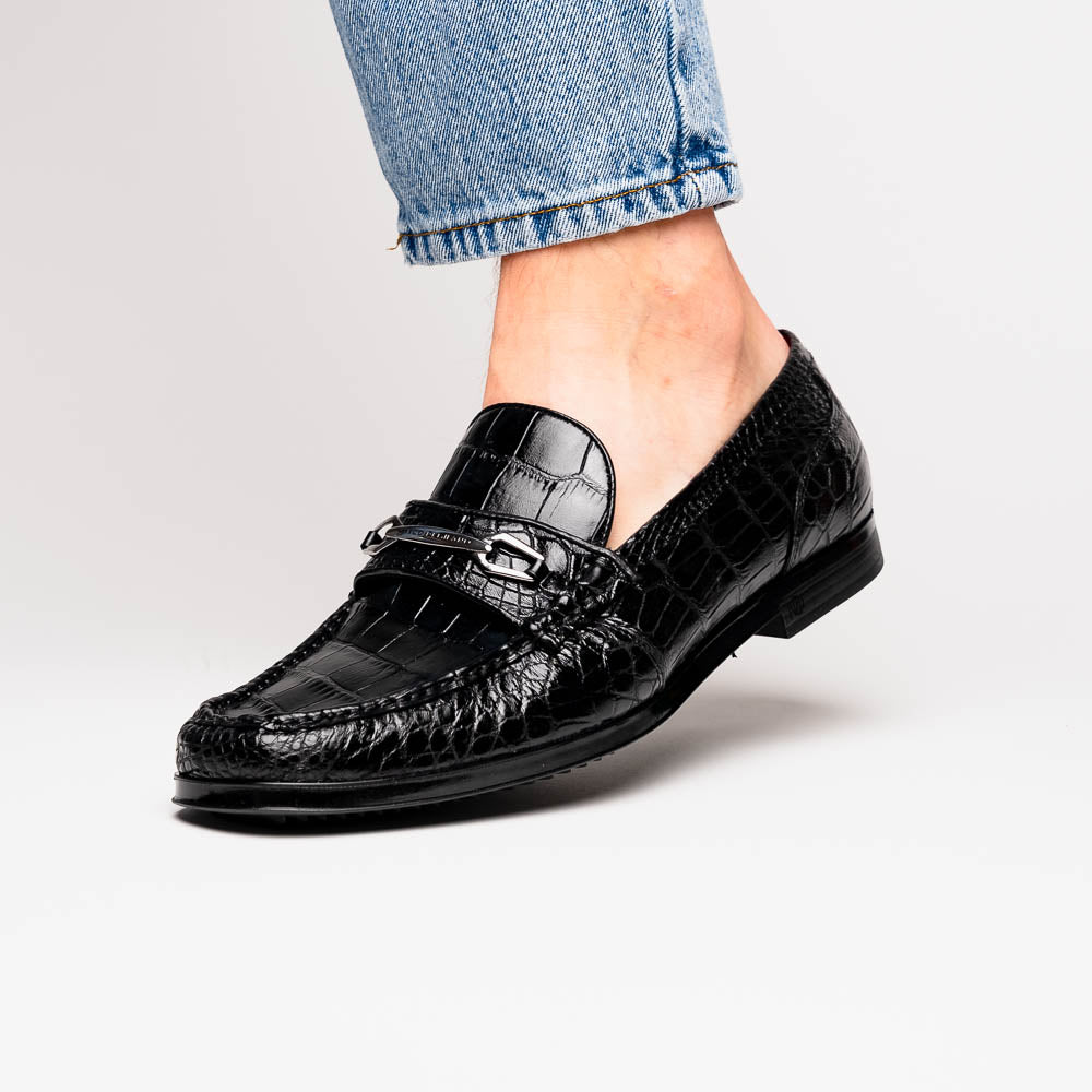 The Milan Black by Marco Di Milano is a black crocodile-pattern leather loafer with a metallic logo detail on the strap and red interior lining, epitomizing luxury men’s footwear.