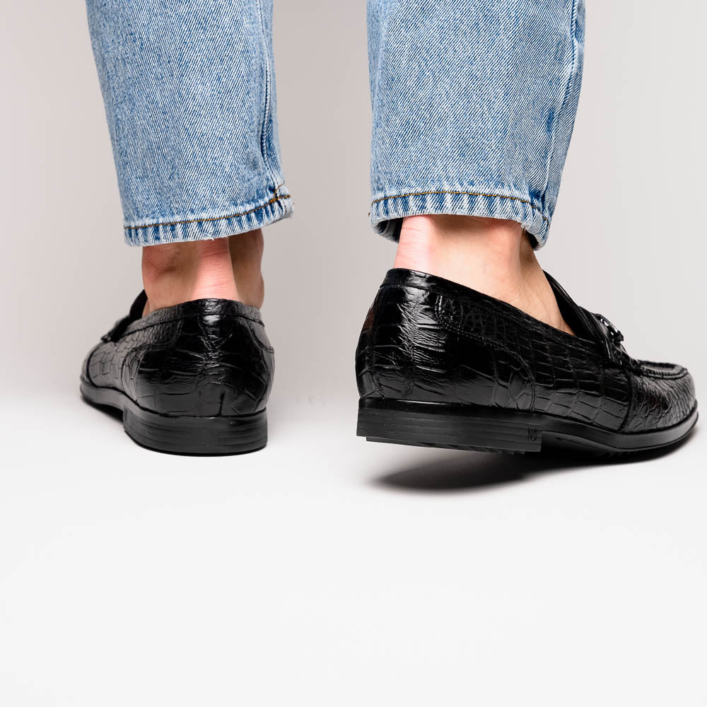 The Milan Black by Marco Di Milano is a black crocodile-pattern leather loafer with a metallic logo detail on the strap and red interior lining, epitomizing luxury men’s footwear.