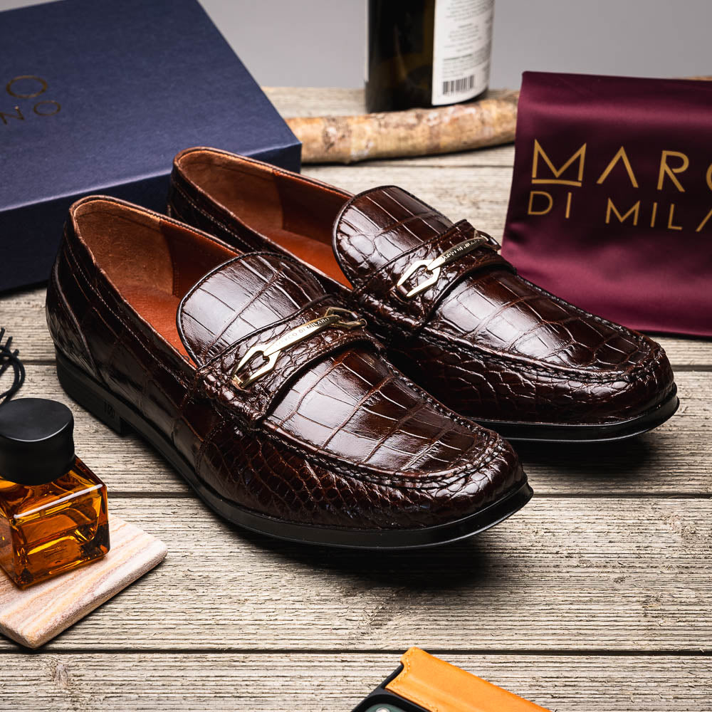 A pair of Marco Di Milano "Milan Brown" luxury loafers featuring brown crocodile-pattern leather and a metal buckle; one shoe is upright while the other is on its side, displaying the sole.
