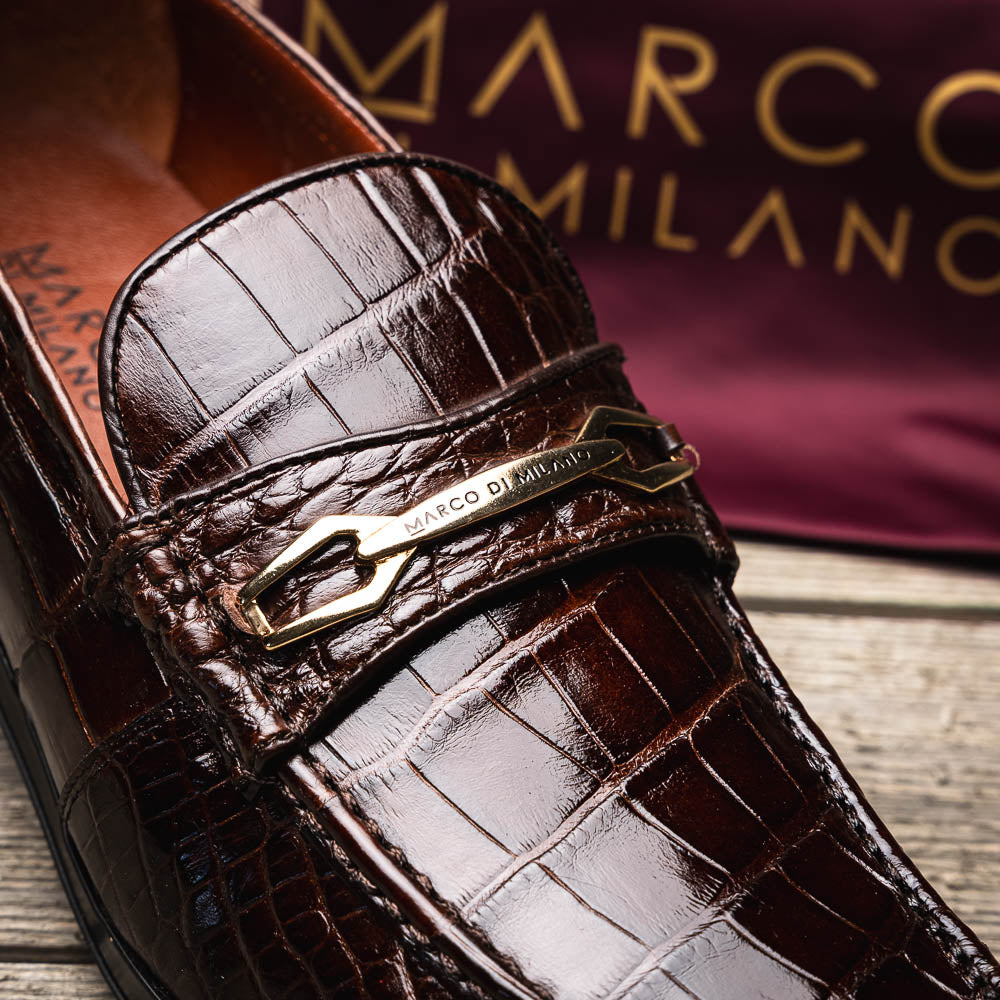 A pair of Marco Di Milano "Milan Brown" luxury loafers featuring brown crocodile-pattern leather and a metal buckle; one shoe is upright while the other is on its side, displaying the sole.