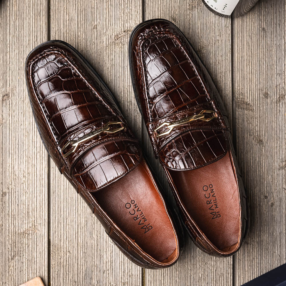 A pair of Marco Di Milano "Milan Brown" luxury loafers featuring brown crocodile-pattern leather and a metal buckle; one shoe is upright while the other is on its side, displaying the sole.