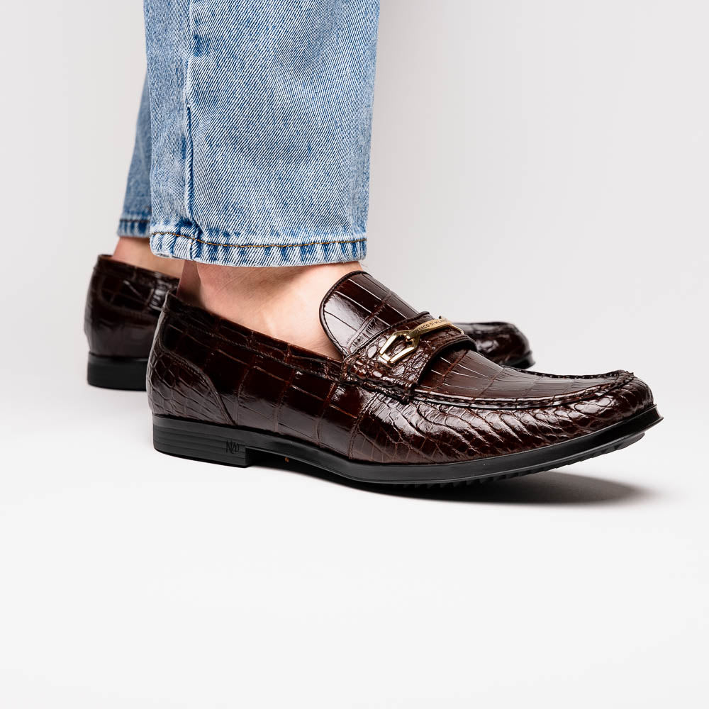 A pair of Marco Di Milano "Milan Brown" luxury loafers featuring brown crocodile-pattern leather and a metal buckle; one shoe is upright while the other is on its side, displaying the sole.