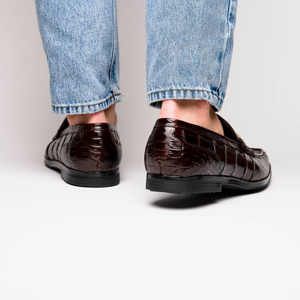 A pair of Marco Di Milano "Milan Brown" luxury loafers featuring brown crocodile-pattern leather and a metal buckle; one shoe is upright while the other is on its side, displaying the sole.