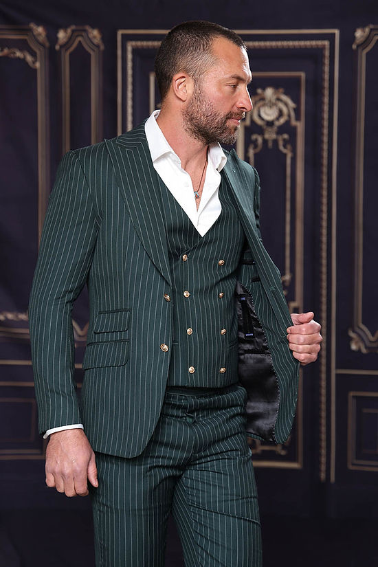 A man in an Insomnia MUCCLY 3PC Modern Fit Hunter Thin Pinstripe Suit with a white shirt stands against an ornate dark background, looking right and adjusting his jacket.