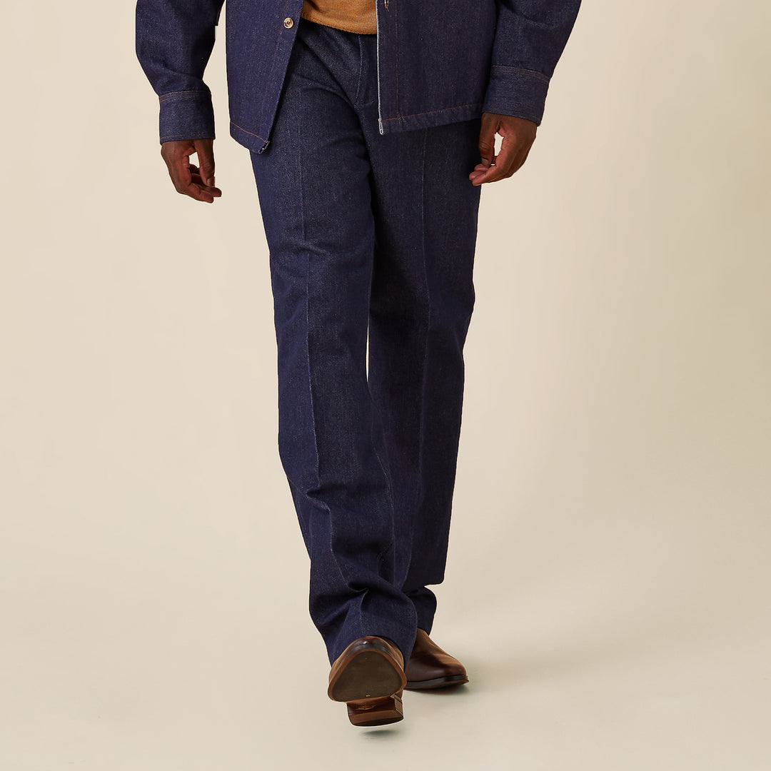 A person wearing Inserch Denim Pants P003-10 Denim Blue with a regular fit dark denim jacket and black and white sneakers, standing against a plain beige background.