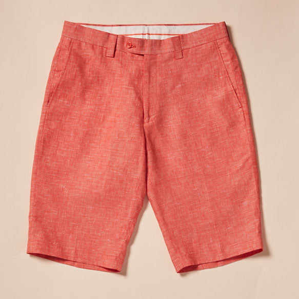 A pair of Inserch Premium Linen Flat Front Shorts in Tangy Orange, reminiscent of vibrant summer wardrobes, lies elegantly on a wood floor.