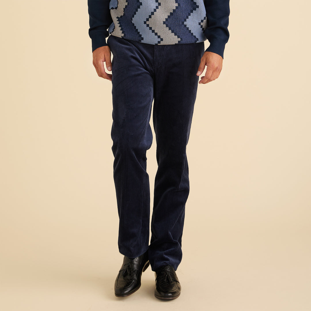 A man smiles with his hands in his pockets, wearing the Inserch Corduroy 4-Pkt Suit BL267-11 in navy blue over an orange and navy patterned sweater.