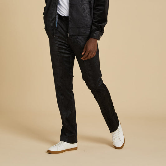 Wearing Inserch Suede Snake Skin Pants P268S-01 Black, a black jacket, and white sneakers, a person stands against a plain beige background.