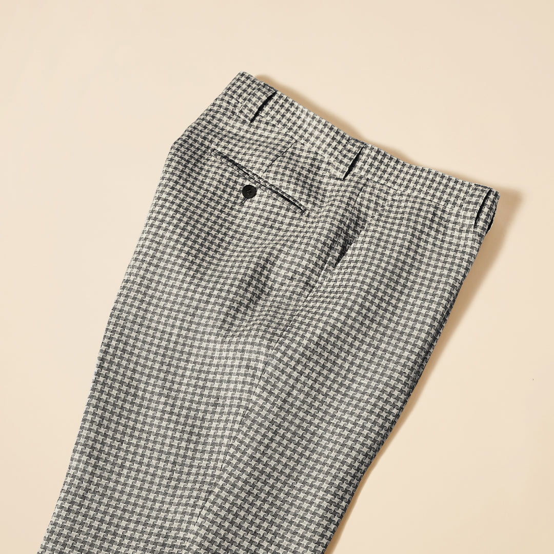 A man confidently walks towards the camera against a plain background, wearing the Inserch Linen Houndstooth Jacket (JS269-00041 Black & White) featuring a sleek 2-way zipper, paired with a black shirt, white pants, and white sneakers.