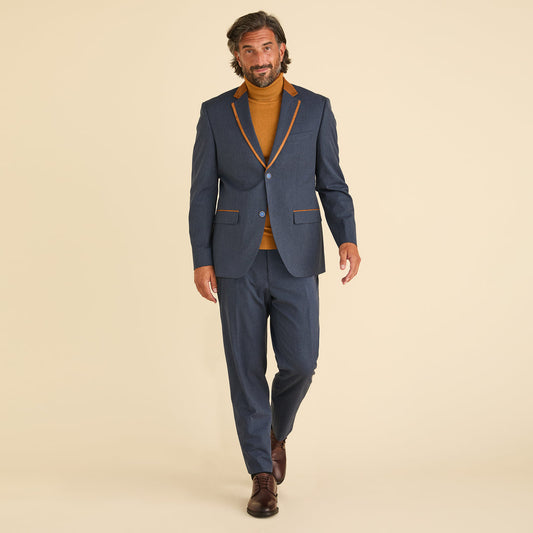 A man in a blue suit with brown trim, mustard turtleneck, and brown dress shoes stands against a beige background, showcasing Inserch Chambray Pants P274-10 Denim Blue by Inserch.