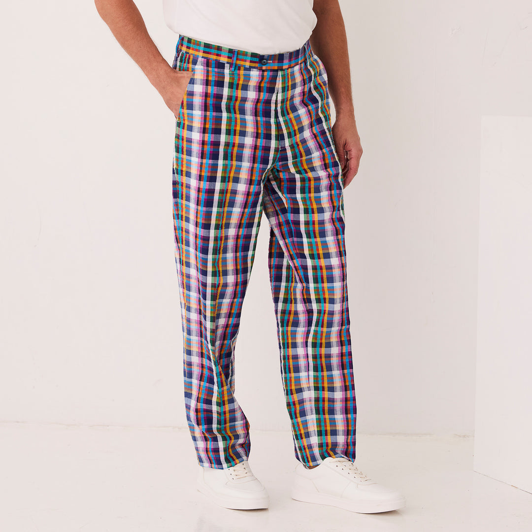 A person wears Inserch Seersucker Plaid Pants P276-00066 Multicolor, crafted from premium cotton. In a neutral-colored room, only their lower half is visible, highlighting the modern fit of these vibrant pants paired with a white shirt.