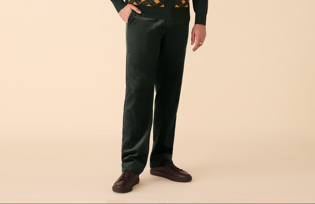 Man wearing a dark green patterned sweater with hunter green pants on a beige background
