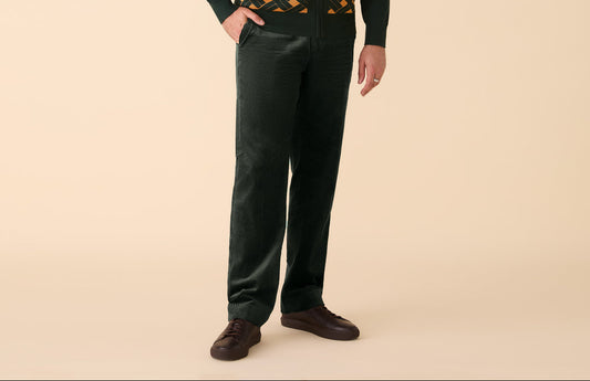 Man wearing a dark green patterned sweater with hunter green pants on a beige background