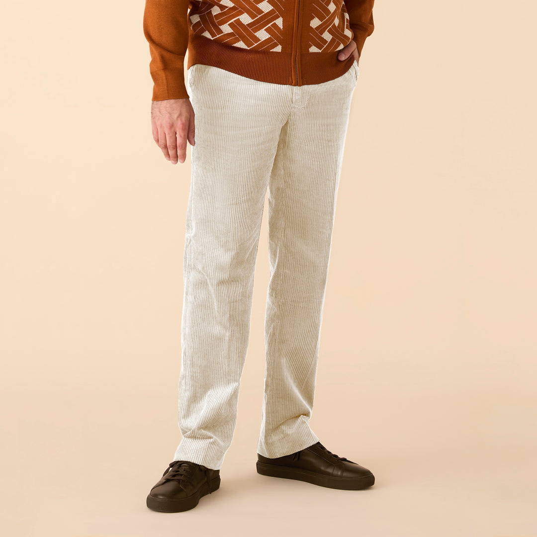 A person wearing Inserch Cotton Corduroy Pants P3103-134 Bone, a modern fit by Inserch, paired with a patterned brown jacket and dark brown shoes, stands against a beige background.