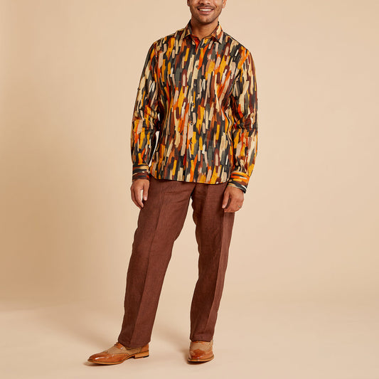A person stands against a beige background wearing a patterned shirt with orange, brown, and black colors, paired with Inserch Linen Pants P3116-00024 Chocolate and modern fit brown leather shoes.