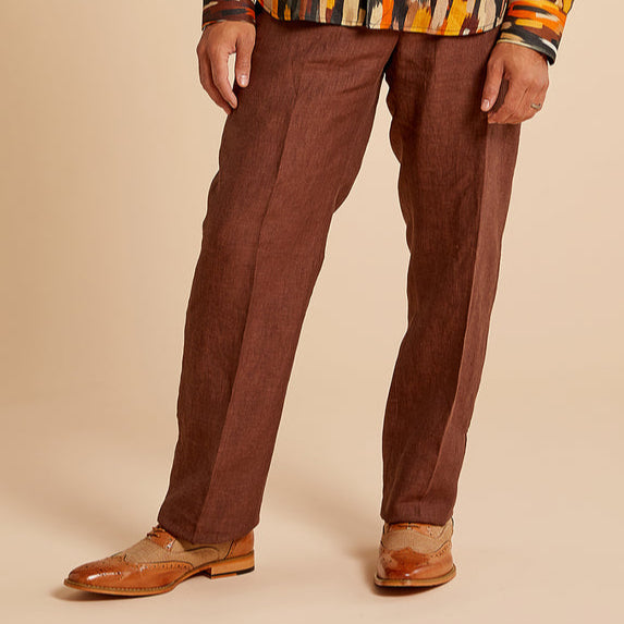 A man smiles in an Inserch Linen 2pc Set (SS717) Chocolate, featuring a patterned long-sleeve shirt and matching pants, paired with tan dress shoes, against a beige background.