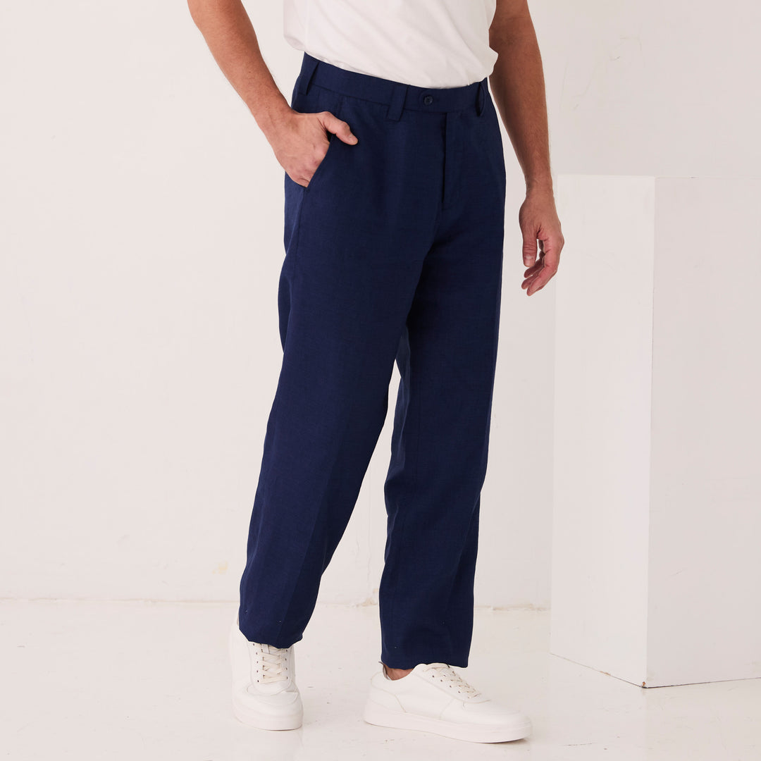 A person wearing a white shirt, Inserch Linen Pants P3116-00036 Ink tailored from European flax, and white sneakers stands with one hand in their pocket against a plain background.