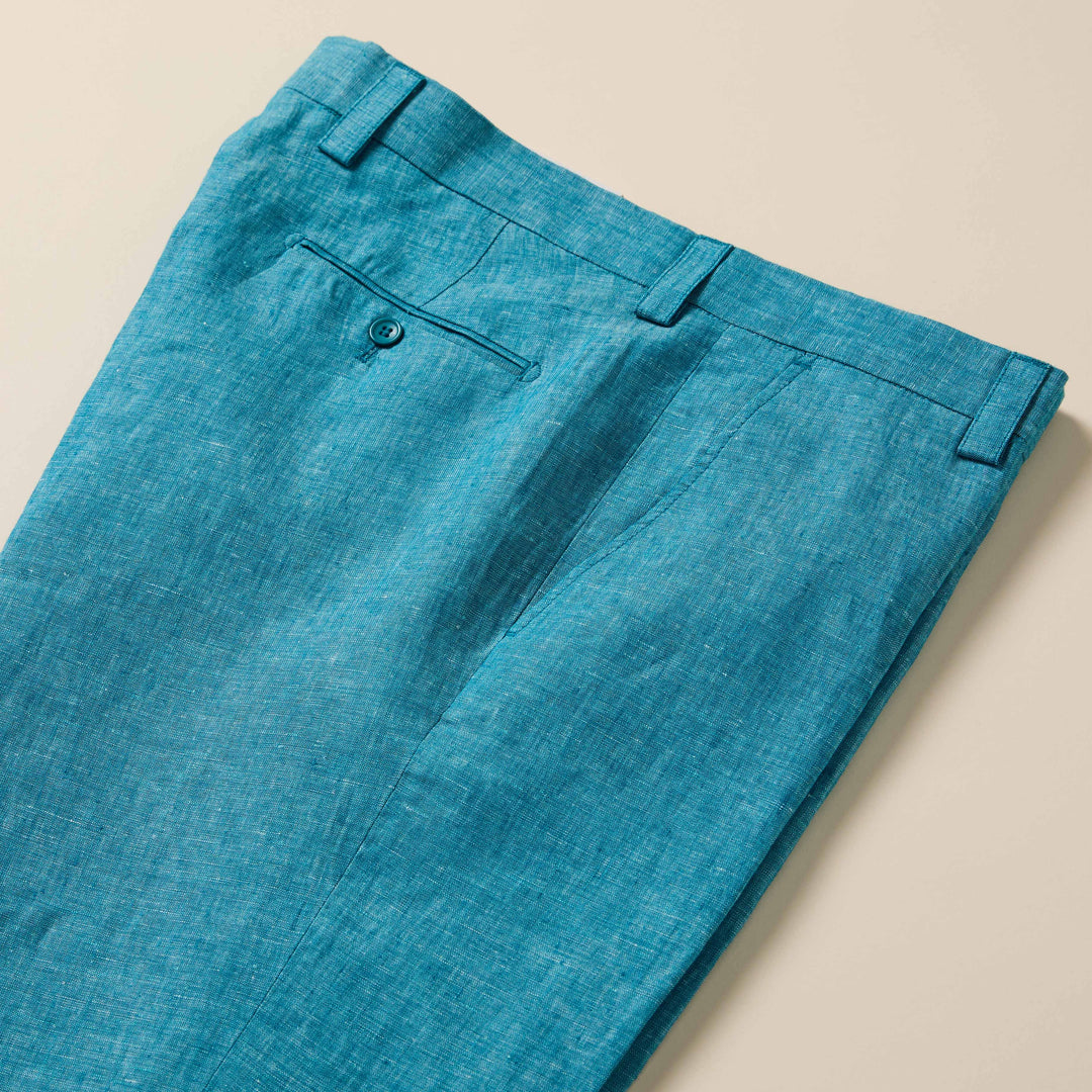 Inserch Linen Pants P3116-00172 Caspian by Inserch: teal blue European flax linen pants with back button pocket, belt loops, and visible seams, shown laid flat on a beige surface.