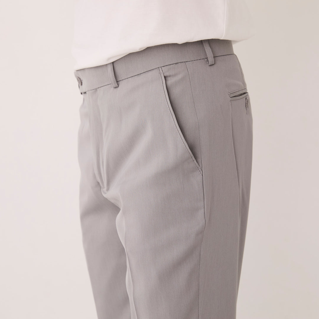 A model wears Inserch Crepe Flat Front Pants P3156-00033 Grey with a white shirt, shown waist to mid-thigh, one hand in the pocket. The poly-crepe fabric is machine washable cold for easy care by Inserch.