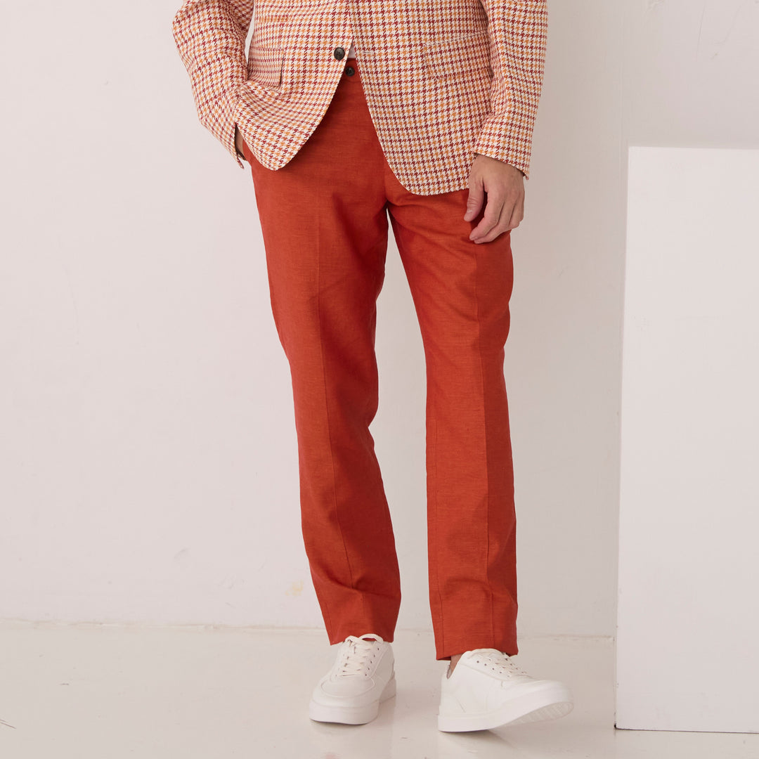 A person wears Inserch Linen Pants P31-00035 Rust, a checkered blazer, and white sneakers while standing against a white background.