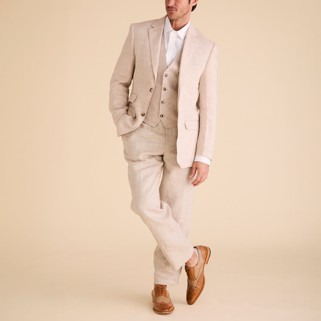 A man wearing Inserch Linen Pants P31-00048 Natural with a matching light beige suit, white dress shirt, and brown dress shoes stands against a neutral background, one leg crossed over the other.