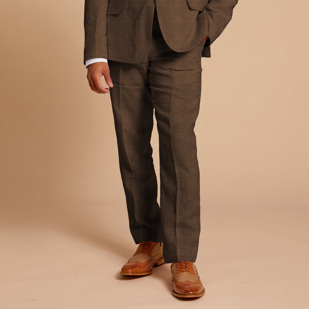 A person wearing Inserch Linen Pants P31-00064 Mocha, a premium linen shirt, and brown brogue shoes stands against a beige background.