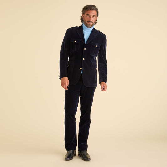 A man stands against a beige background wearing the Inserch Velvet Military Suit BL569-11 Navy Blue, paired with a light blue turtleneck and black shoes.