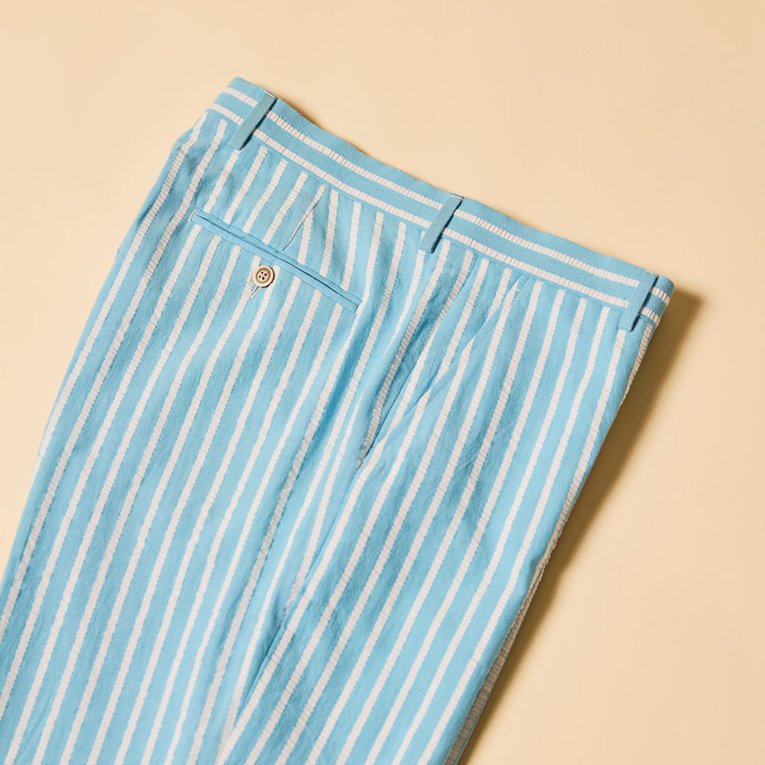A person wears the Inserch Seersucker Wide Stripe Pants P507-00183 in Blue Mist, paired with tan dress shoes, standing against a beige background.