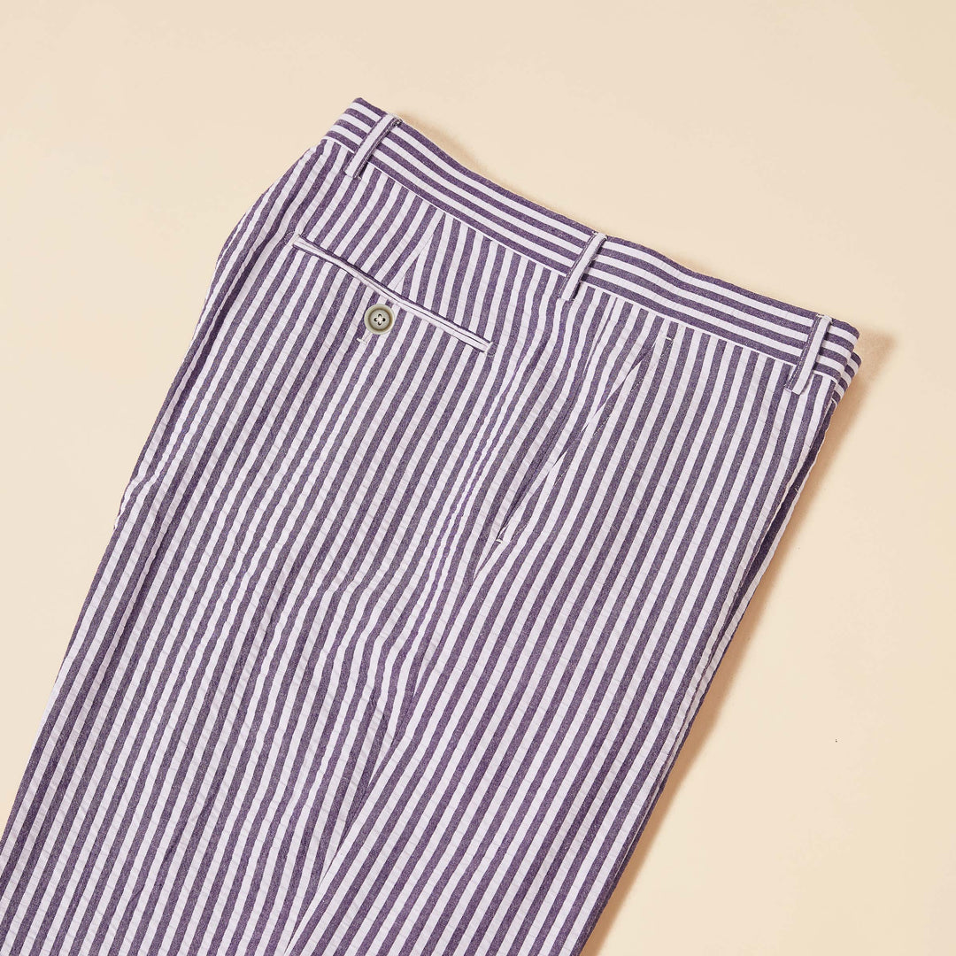 The Inserch Seersucker Stripe Pants (P660155-00068 Eggplant) lie on a beige surface, showcasing belt loops and a buttoned back pocket. Made from premium cotton, they offer a modern fit.
