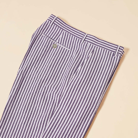 The Inserch Seersucker Stripe Pants (P660155-00068 Eggplant) lie on a beige surface, showcasing belt loops and a buttoned back pocket. Made from premium cotton, they offer a modern fit.