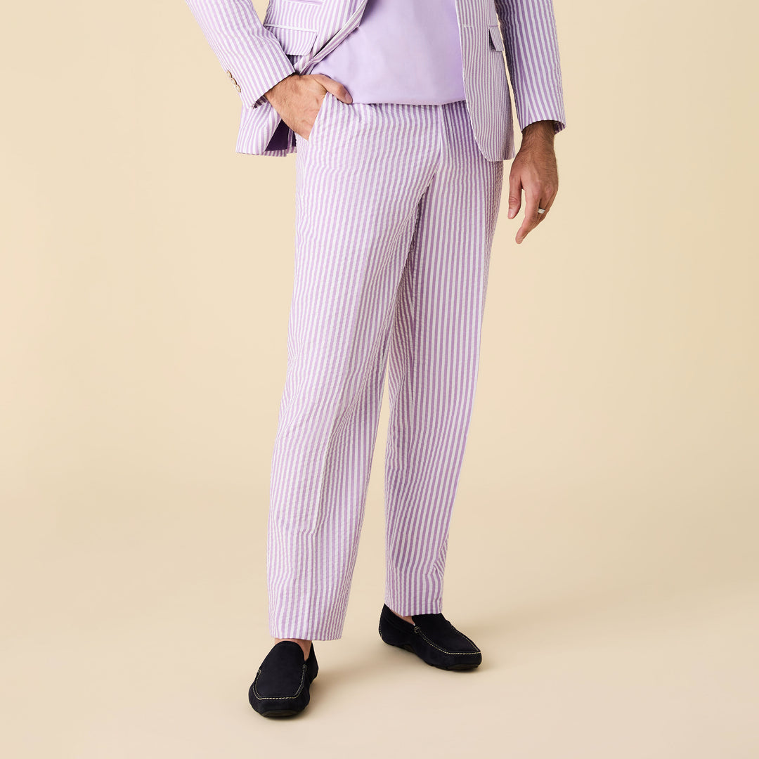 A person stands against a beige background wearing Inserch Seersucker Stripe Pants P660155-00119 Lavender by Inserch, paired with a matching shirt and black slip-on shoes.
