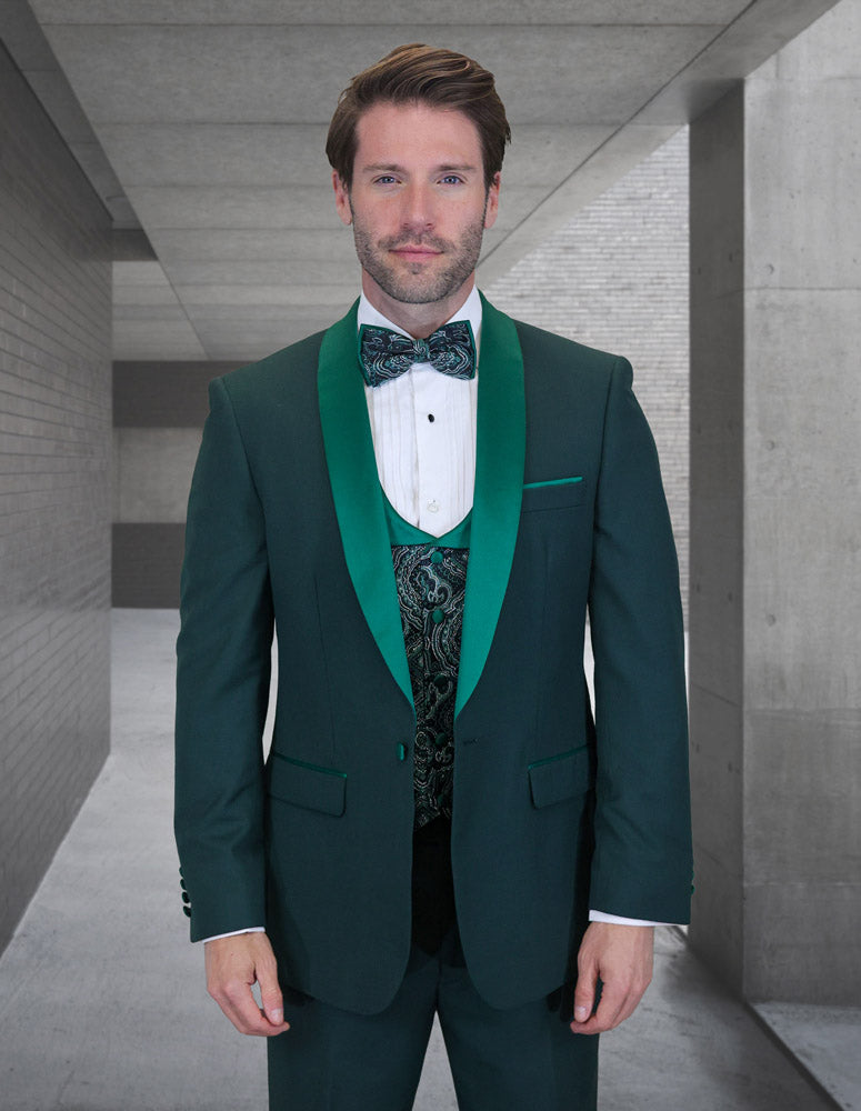 A man wearing the STATEMENT CLOTHING | PALMERO-HUNTER dark green tuxedo by Statement Clothing with a coop neck vest and flat front pants stands in a modern concrete corridor, facing the camera.