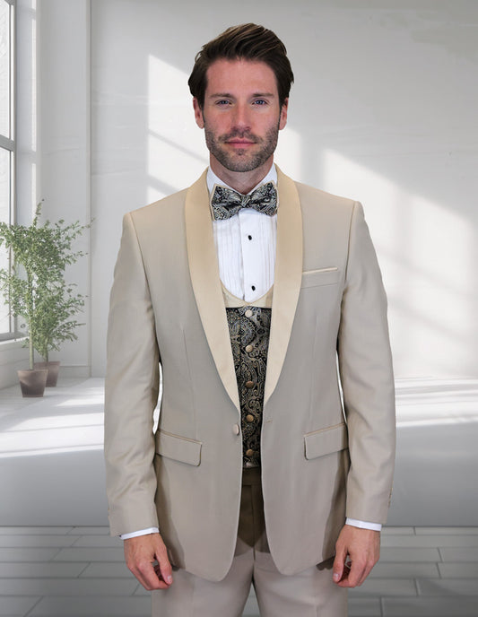 A man wears the STATEMENT CLOTHING | PALMERO-TAN tailored tuxedo by Statement Clothing with a white shirt, patterned vest, and bow tie, standing indoors near a window with natural light and a potted plant.