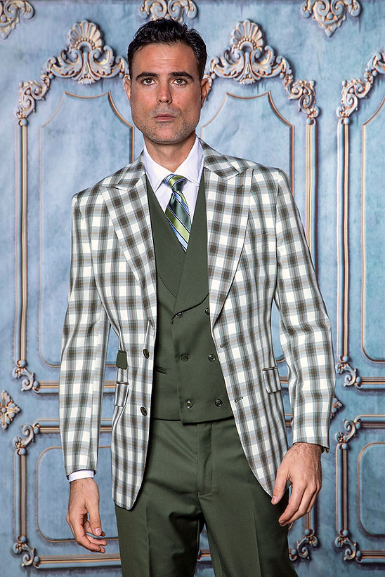 A man wearing the Manzini MANZINI PARIS-4 Men's 3-Piece Tailored-Fit Plaid Business Suit in hunter stands before an ornate light blue and gold patterned wall.