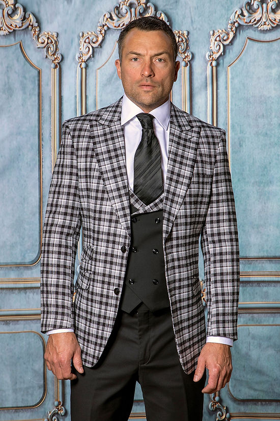 A man in the INSOMNIA PARIS-6 3-Piece Tailored Fit Plaid Formal Business Black Suit by Insomnia stands before an ornate blue and white paneled backdrop, highlighting this refined ensemble.